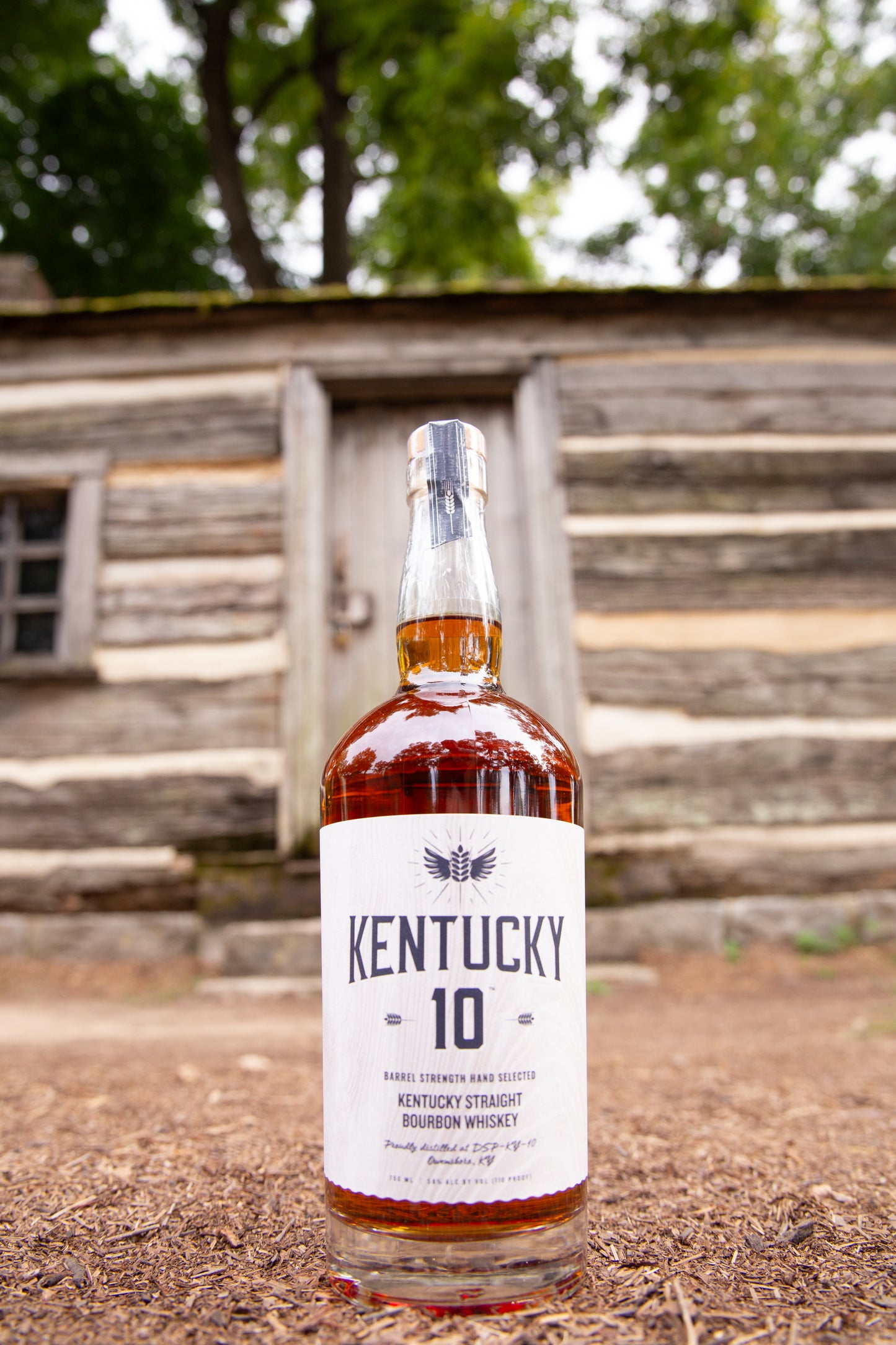 White bottle of Kentucky 10 placed outside by a log cabin