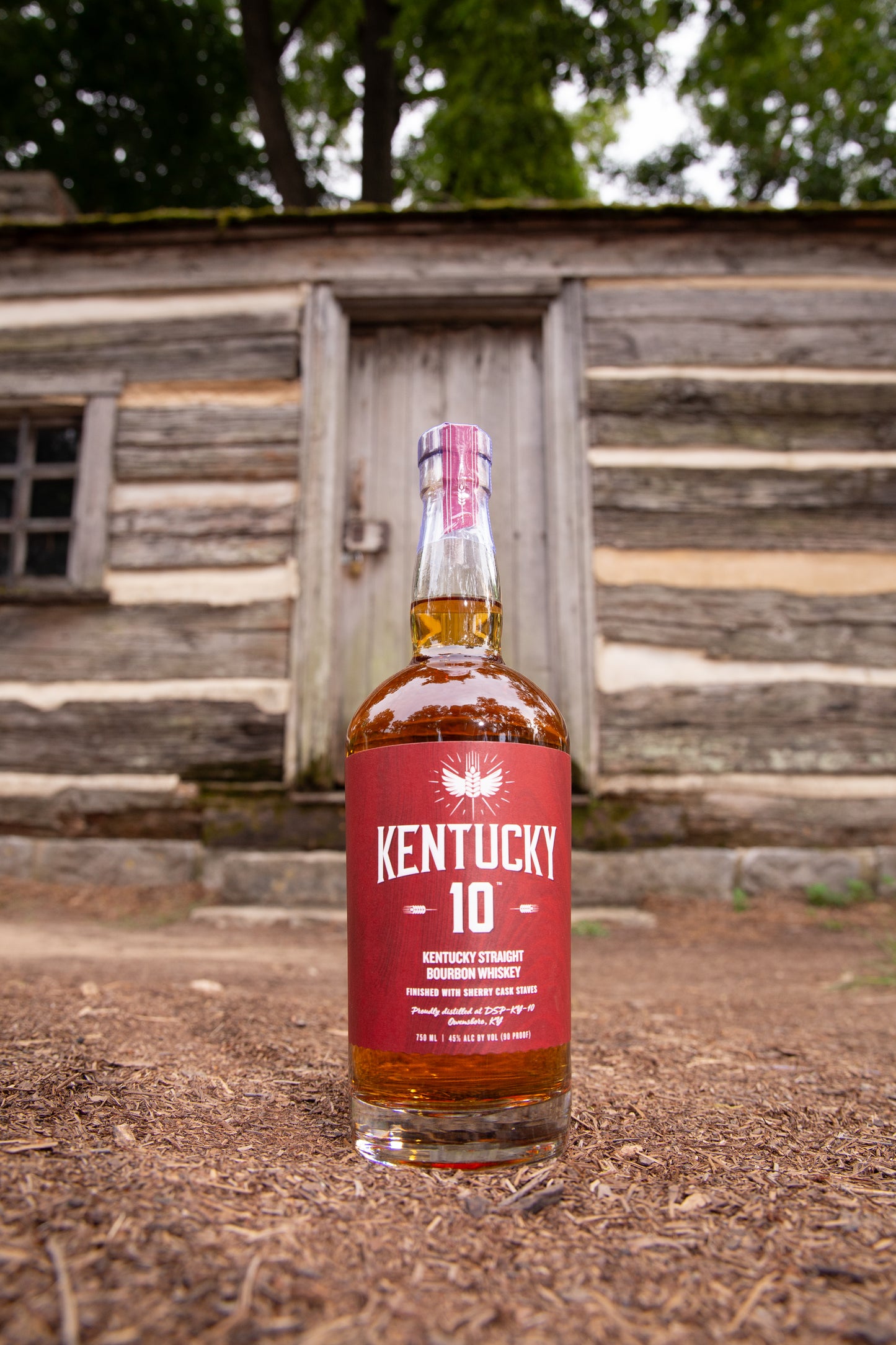 Red bottle of Kentucky 10 placed outside by a log cabin