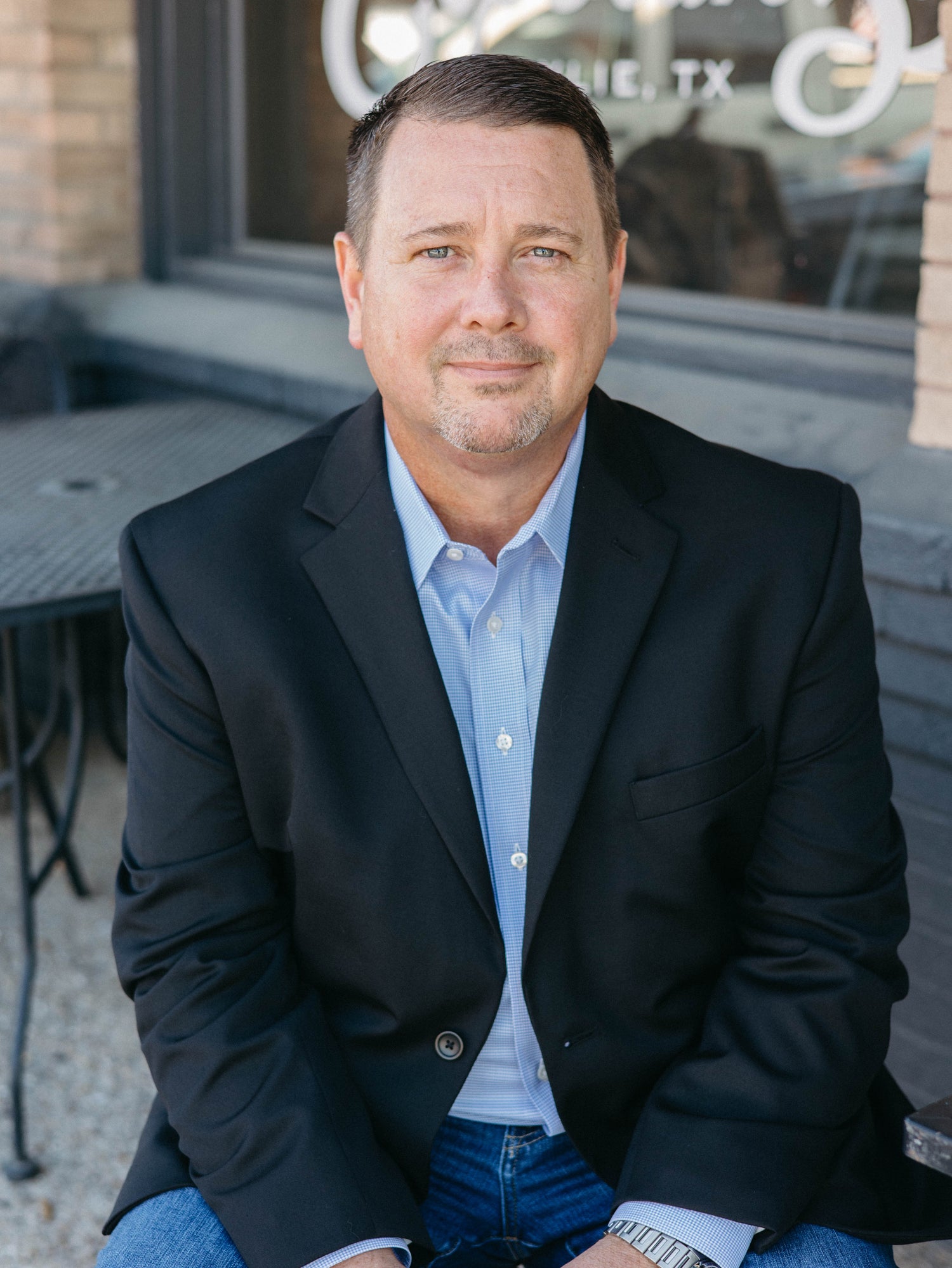 Male Founder sitting for a headshot wearing a blue suit and a paid of jeans