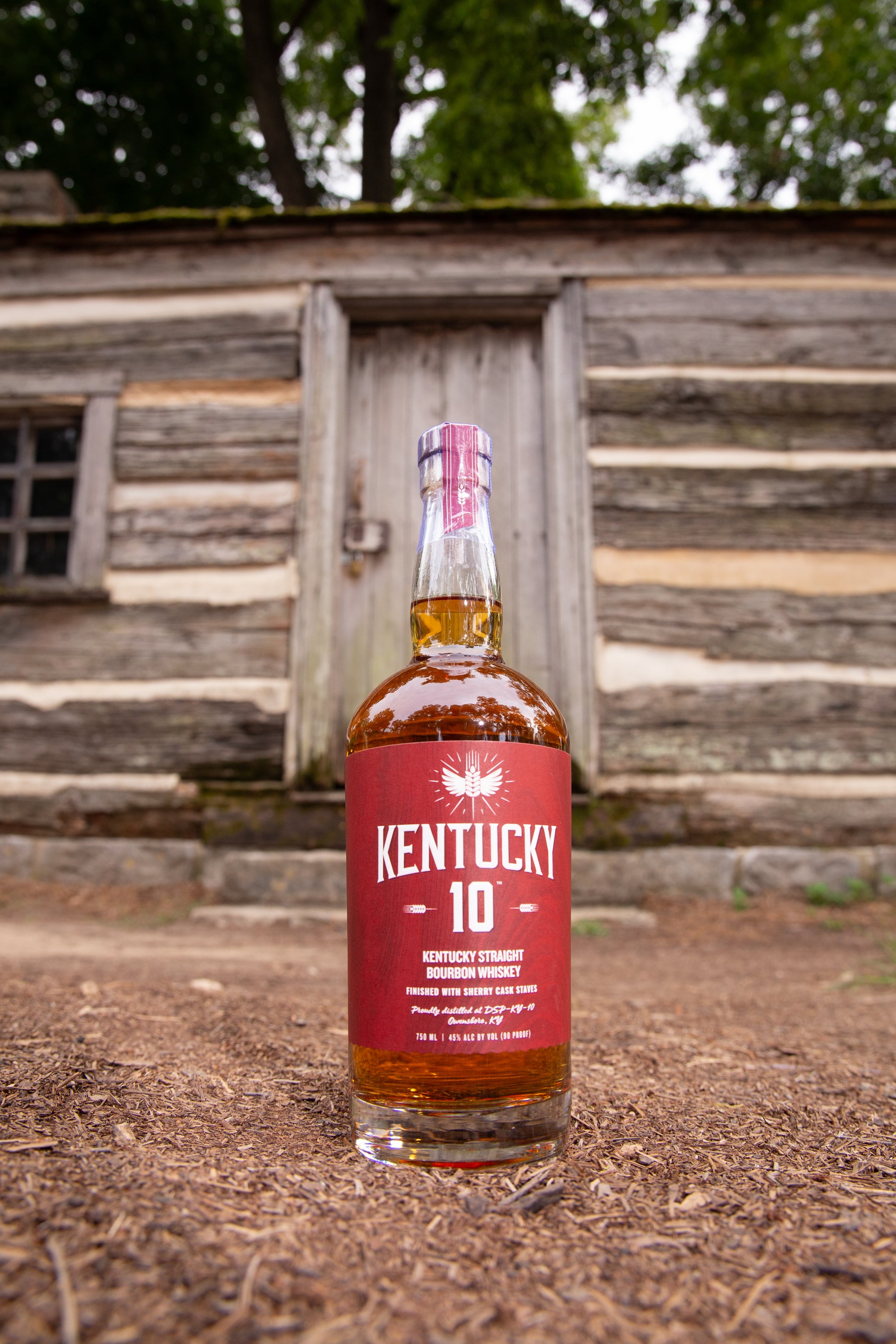 Red bottle of Kentucky 10 placed outside by a log cabin